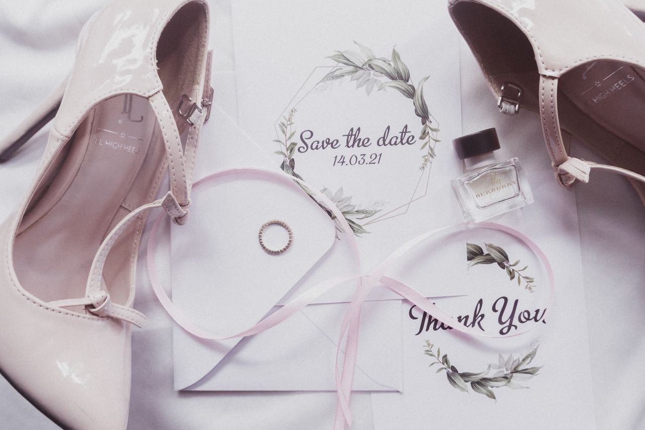 A stylish flat lay of wedding essentials featuring heels, perfume, and invitations.